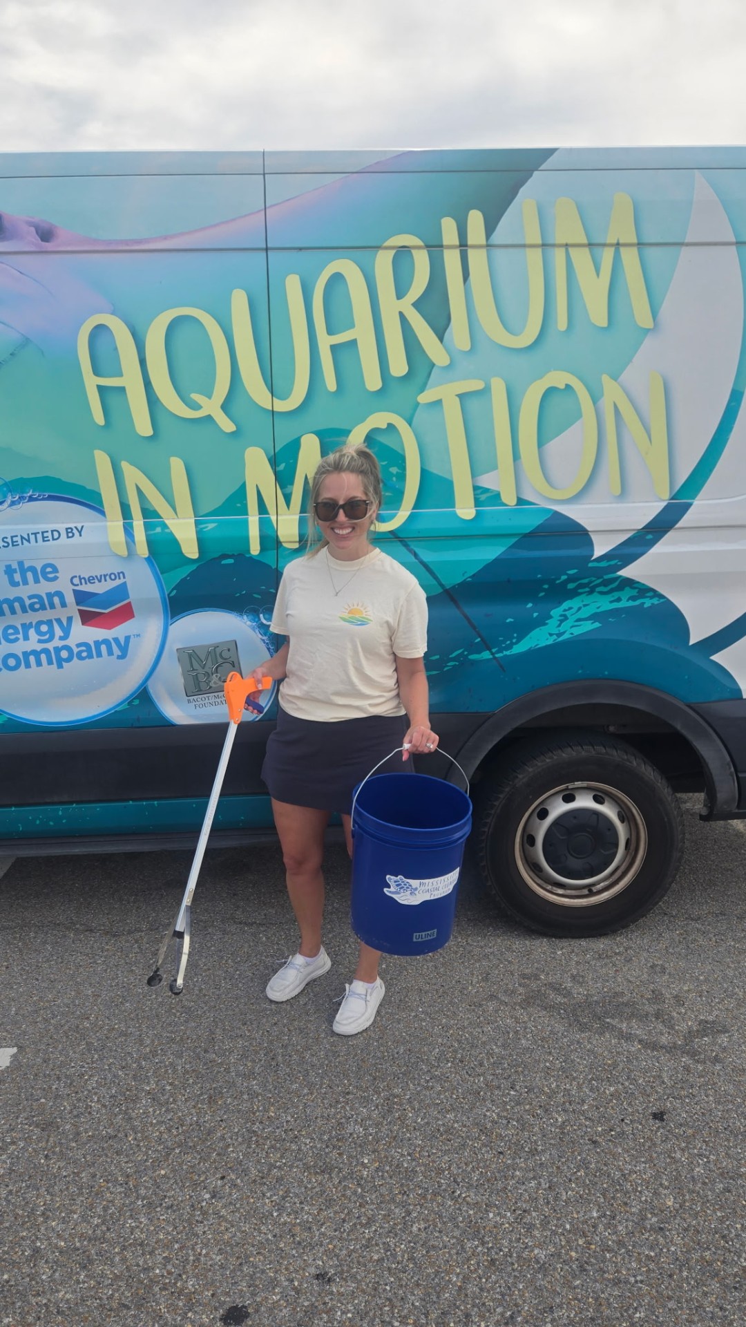 Jenelle volunteering at a Mississippi Aquarium beach cleanup, holding a bucket and litter grabber